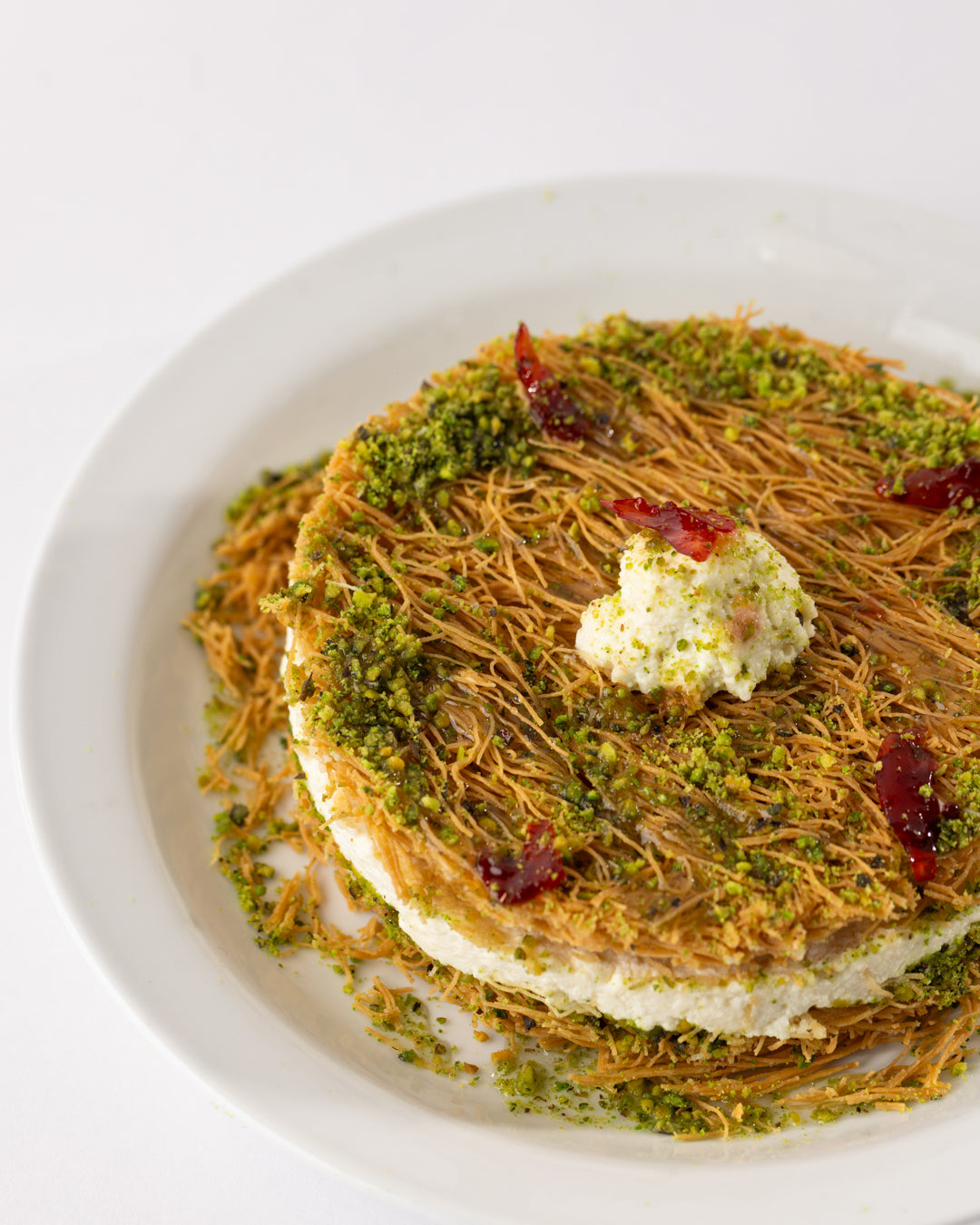 Esmaliye Plate with vermicelli dough, kashta filling, pistachio paste, and a dollop of cream on a white plate.