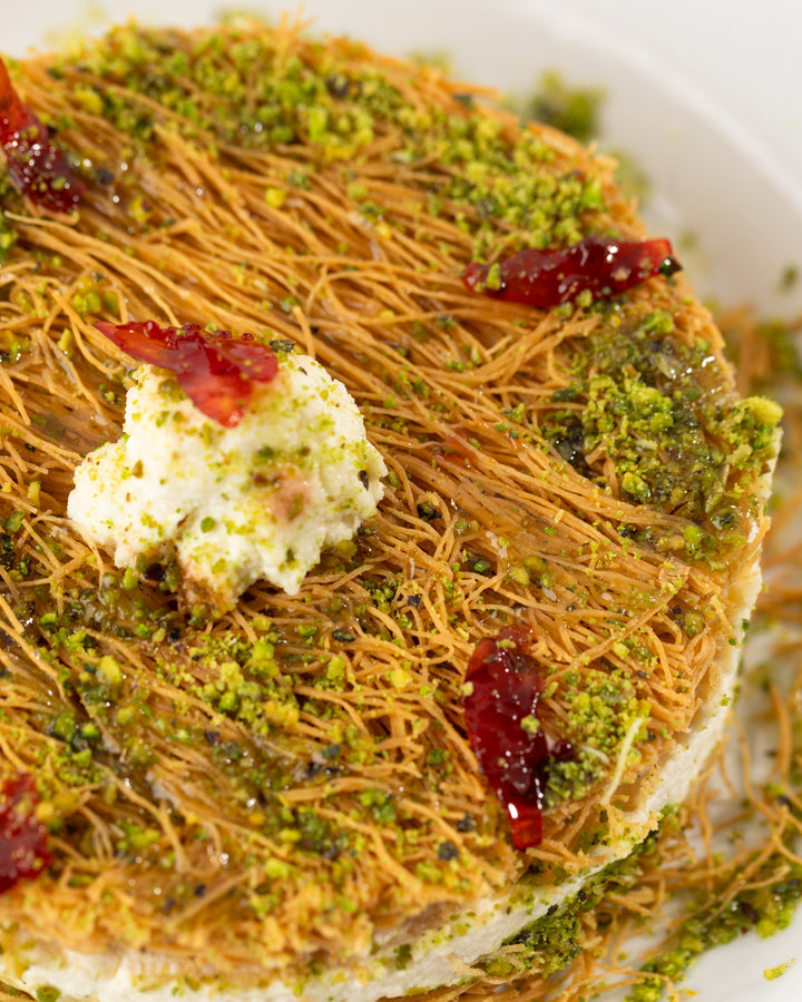 Close-up of Esmaliye Plate dessert topped with pistachio, kashta cream, and pieces of dried fruit on a white plate