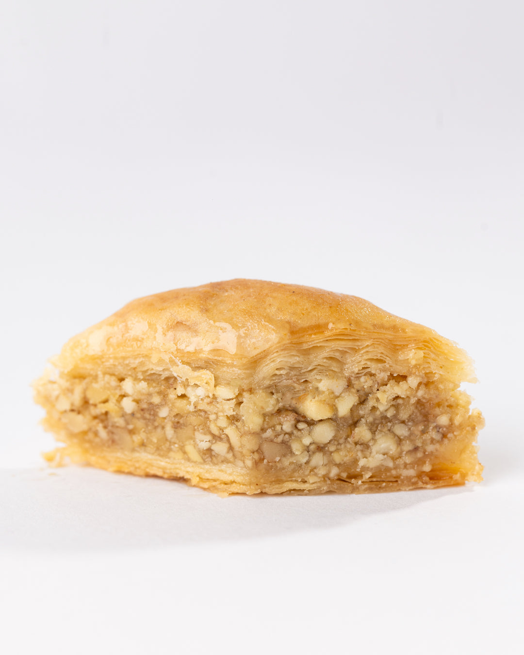 Close-up of syrup-soaked Hadaf Joz pastry filled with crunchy walnuts and flaky layers on a white background