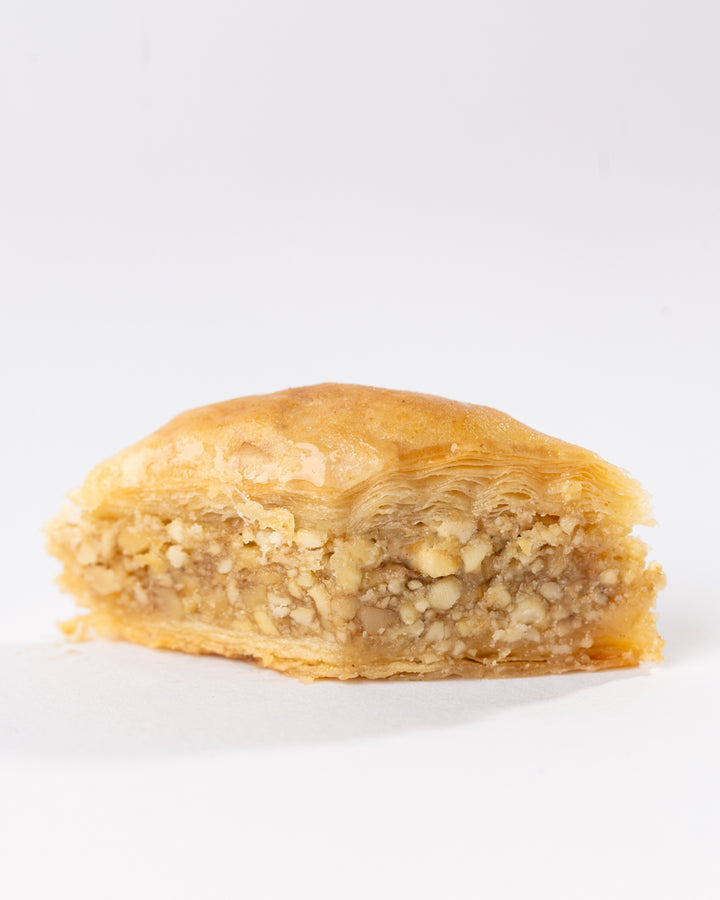 Close-up of syrup-soaked Hadaf Joz pastry filled with crunchy walnuts and flaky layers on a white background