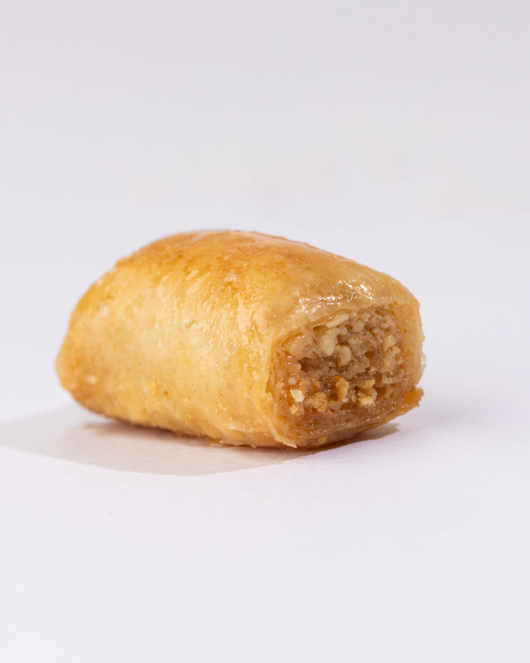 Close-up of a golden Asabih cashew puff pastry filled with crushed cashew nuts and coated in sweet syrup