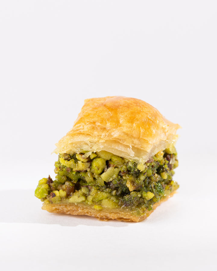 Close-up of Beklewa pistachio pastry with golden puff pastry and crushed pistachio filling on a white background