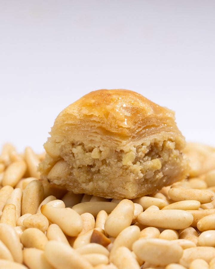 Close-up of Beklewa bl snoubar puff pastry crisp filled with pine nuts and sweet syrup on a bed of pine nuts.