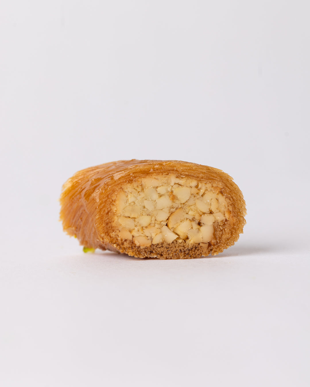 Close-up of Borma cashew dessert showing cashew-stuffed vermicelli dough coated with sugar syrup on white background