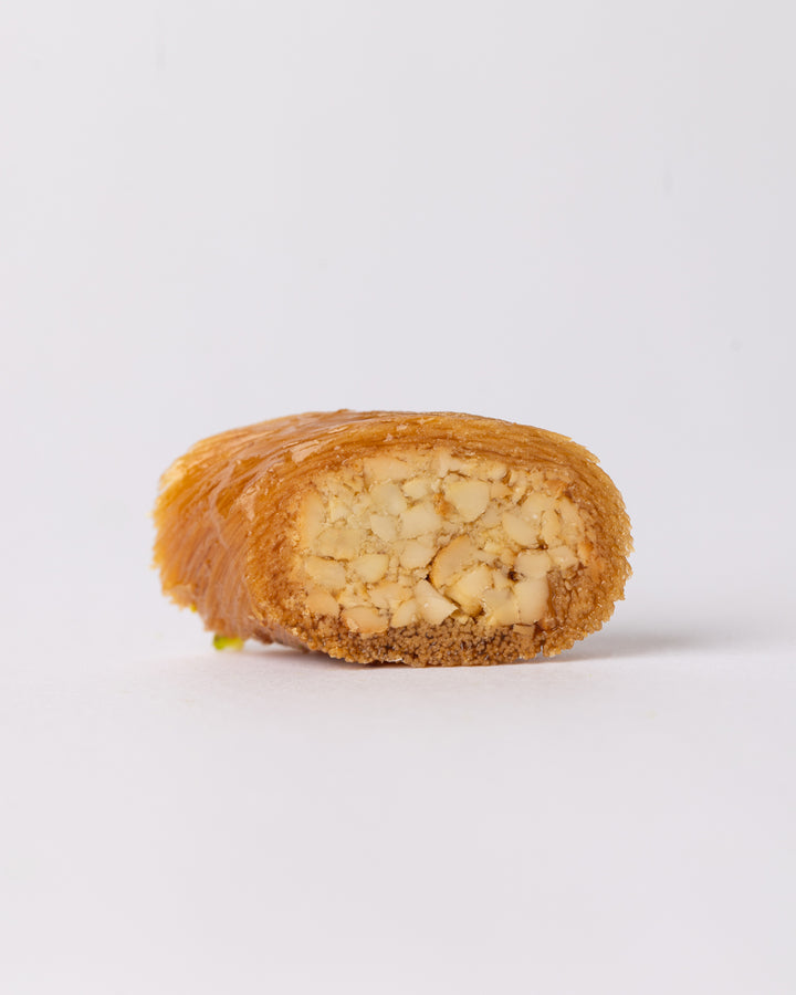 Close-up of Borma cashew dessert showing cashew-stuffed vermicelli dough coated with sugar syrup on white background