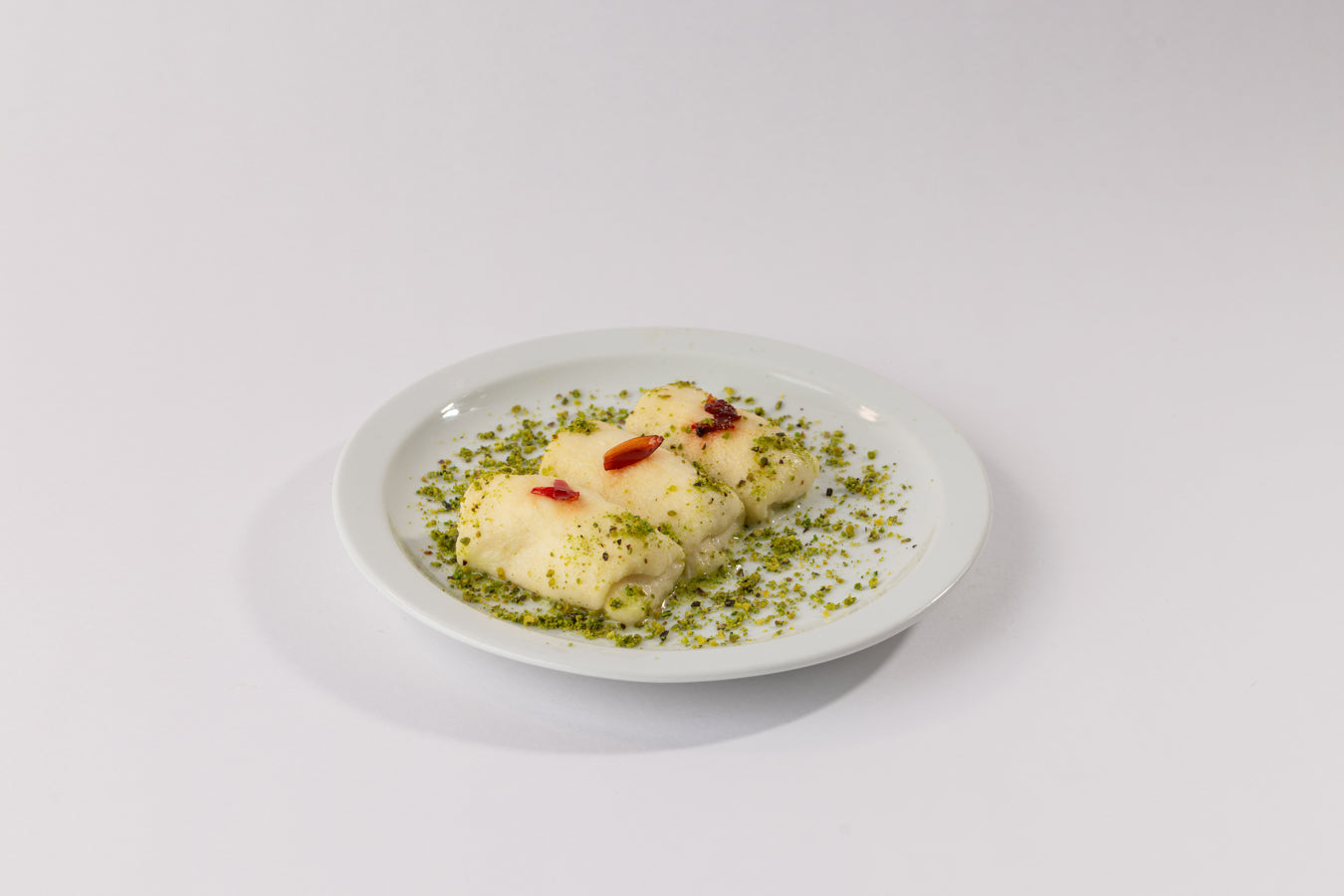 Halewet el Jeben rolls on a white plate topped with creamy kashta, ground pistachios, and flower jam garnished delicately