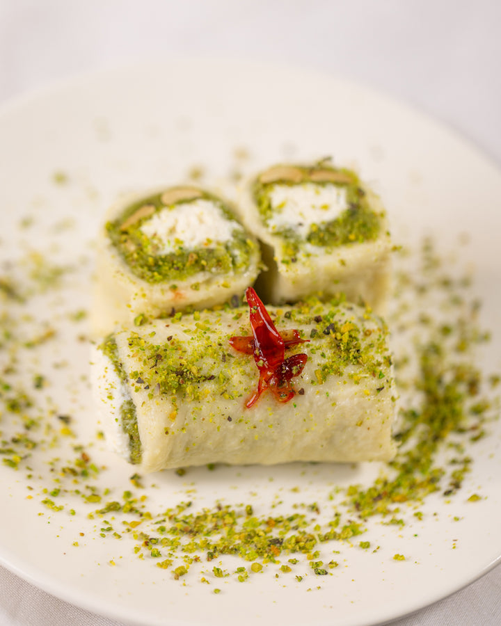 Creamy Halewet el Jeben rolls topped with crushed pistachios and flower jam on a white plate close-up view