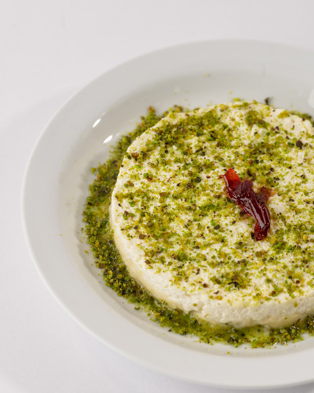Halewit el jeben plate topped with creamy Kashta, ground pistachios, flower jam, and served with sugar syrup on white plate.