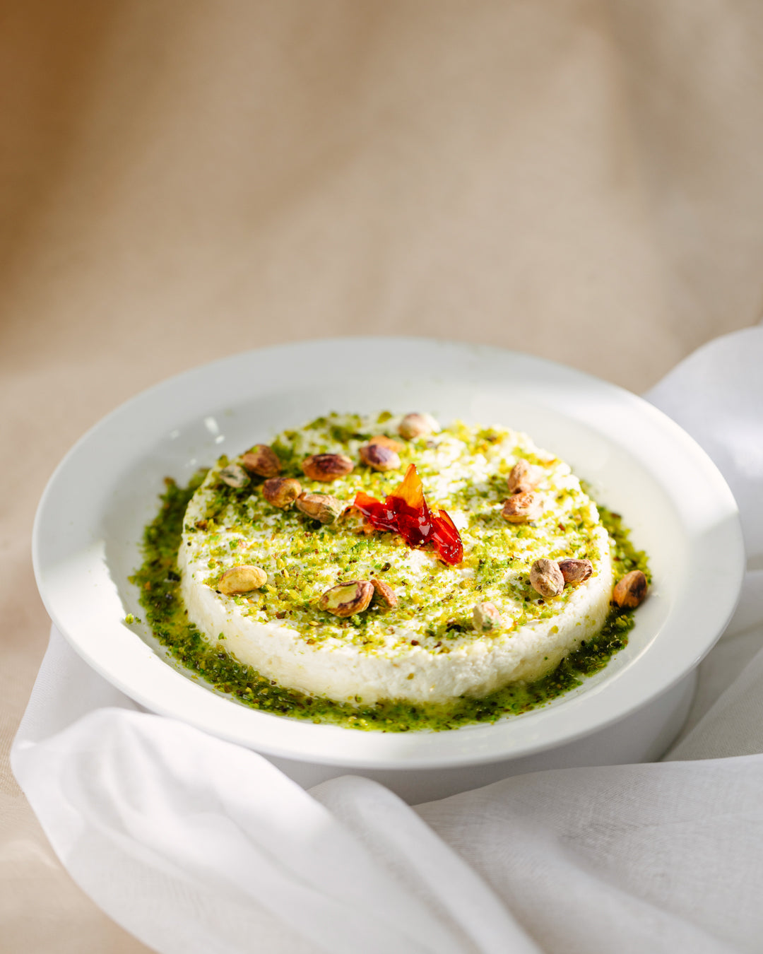 Halewit el jeben plate topped with creamy kashta, pistachios, and flower jam served with sugar syrup on a white plate.