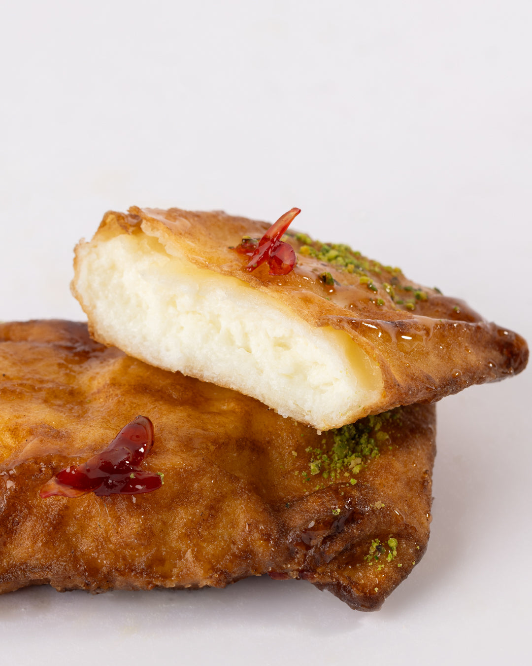 Golden grilled Kellej pastry filled with sweet cheese, garnished with nuts and a drizzle of syrup on a white background.