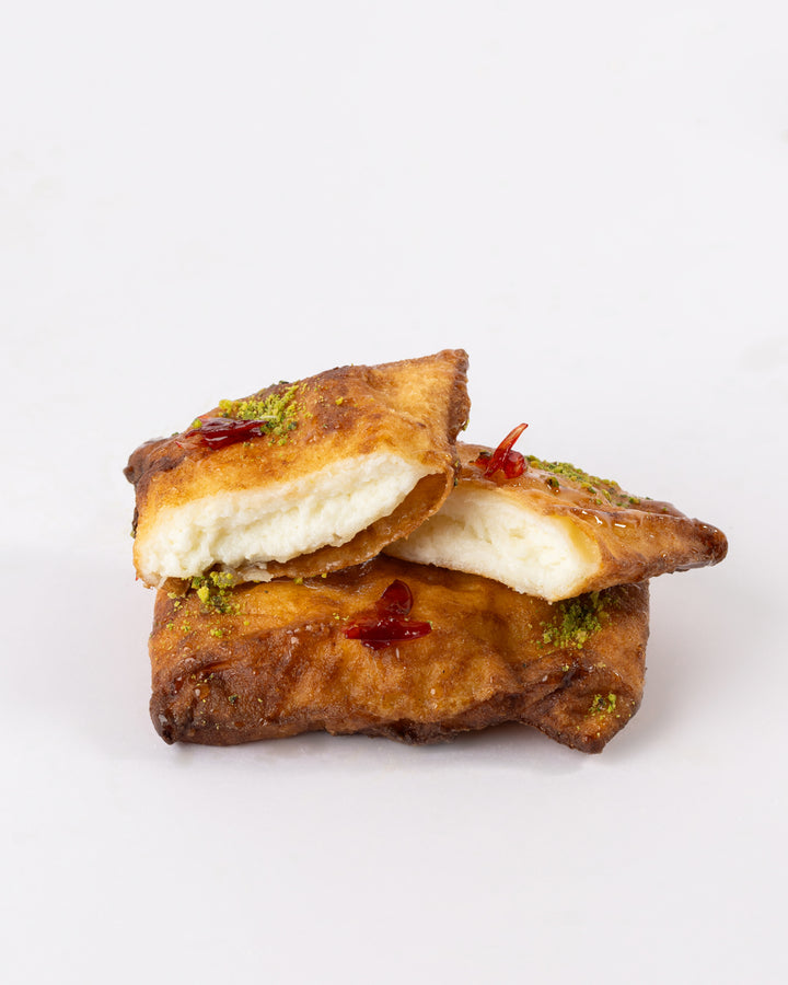 Golden grilled Kellej pastry filled with sweet cheese, garnished with pistachios and a touch of syrup on white background.