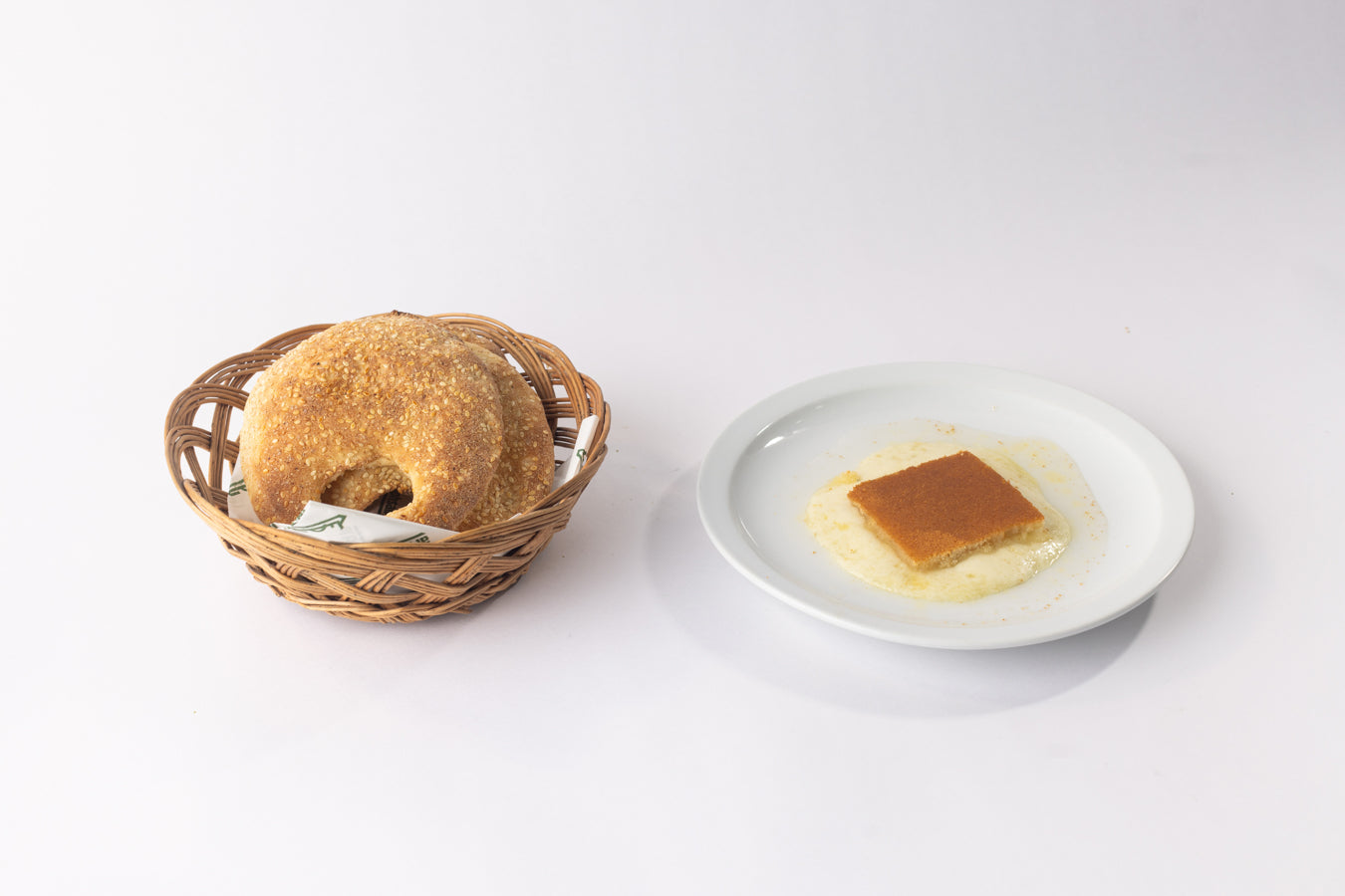 Traditional Lebanese knefe with cheese on a plate beside sesame-coated kaake bread in a basket