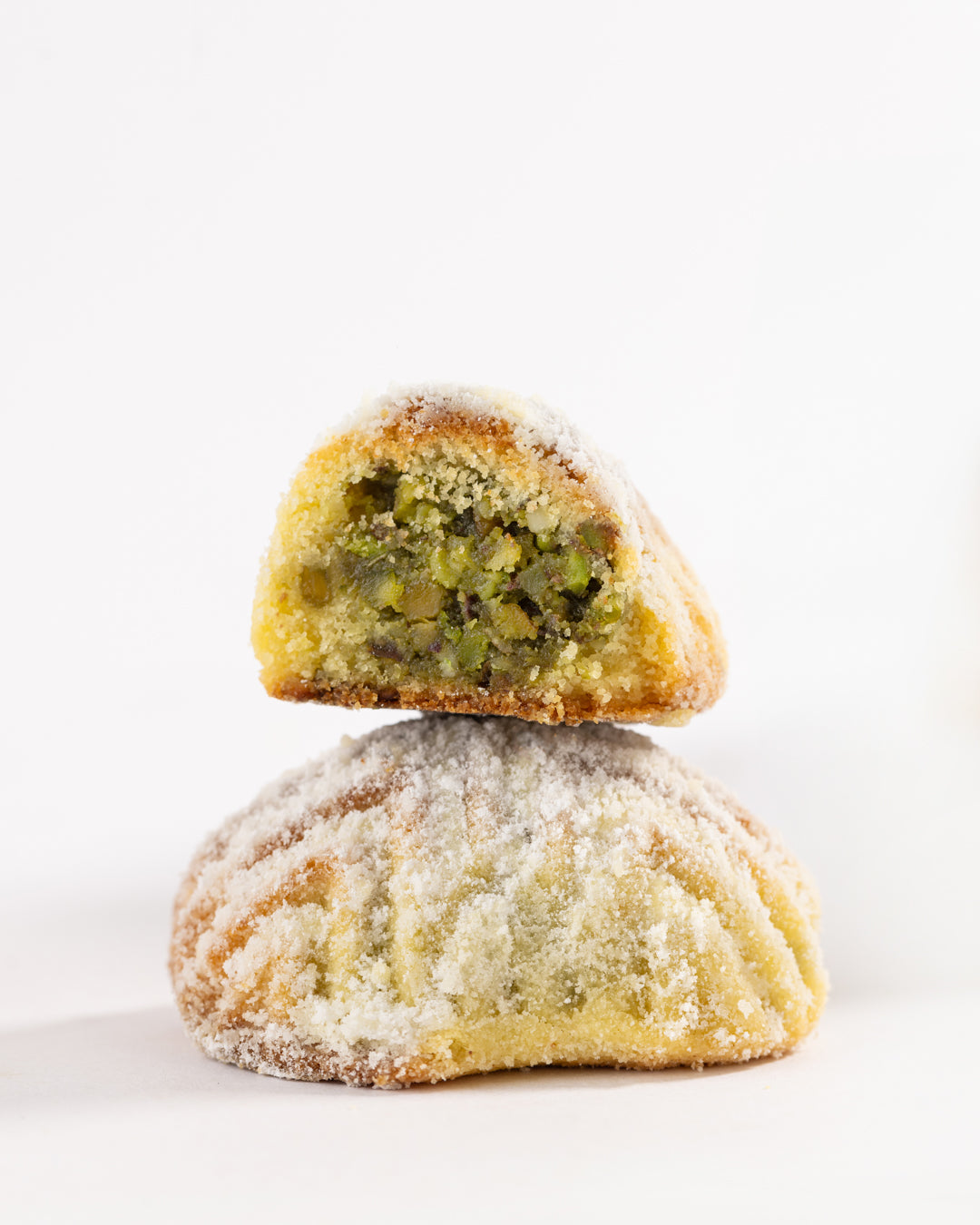 Close-up of Maamoul festok filled with ground pistachios and dusted with fine sugar powder on a white background
