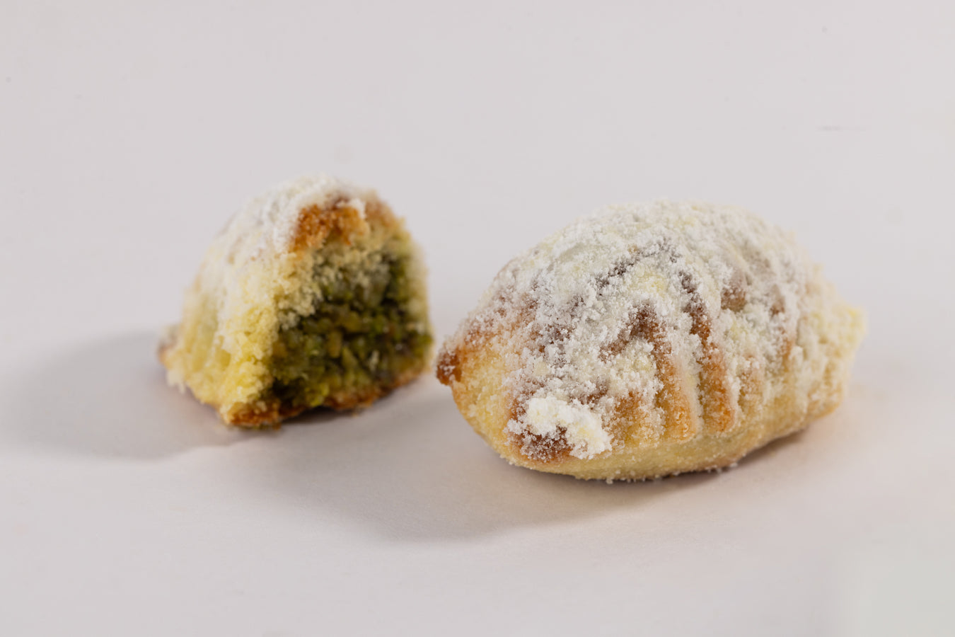 Close-up of Maamoul festok cookies filled with ground pistachios and dusted with powdered sugar on white background