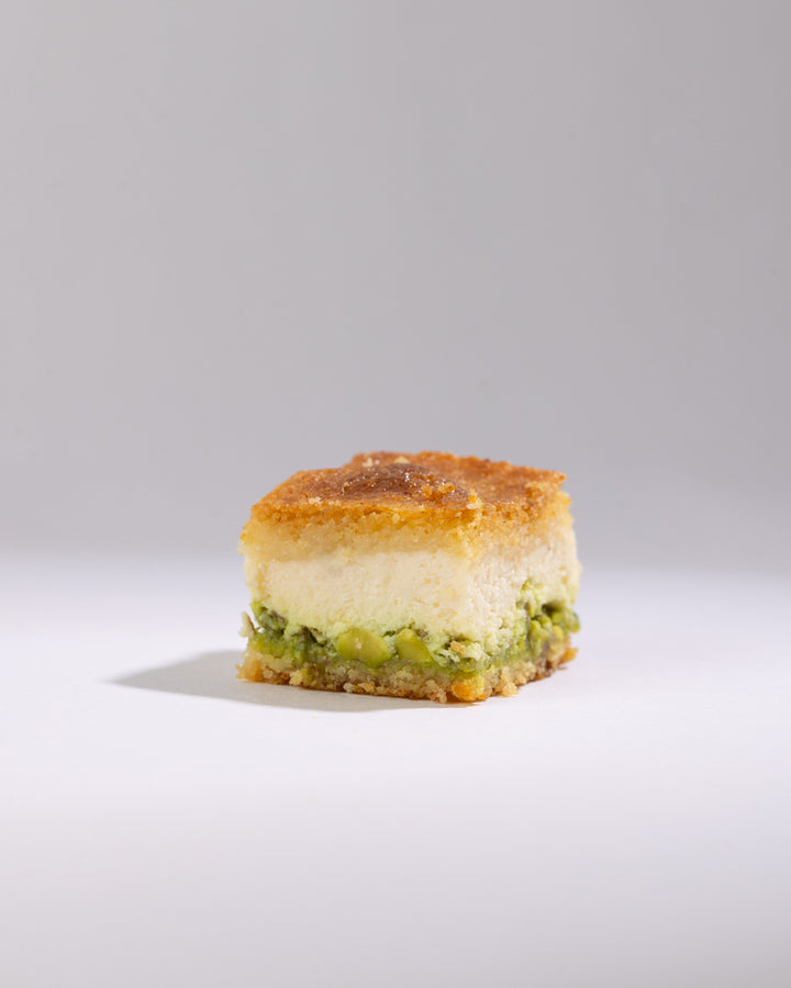 Square piece of Maamoul Mad Kashta dessert with creamy kashta and pistachio filling on a white background