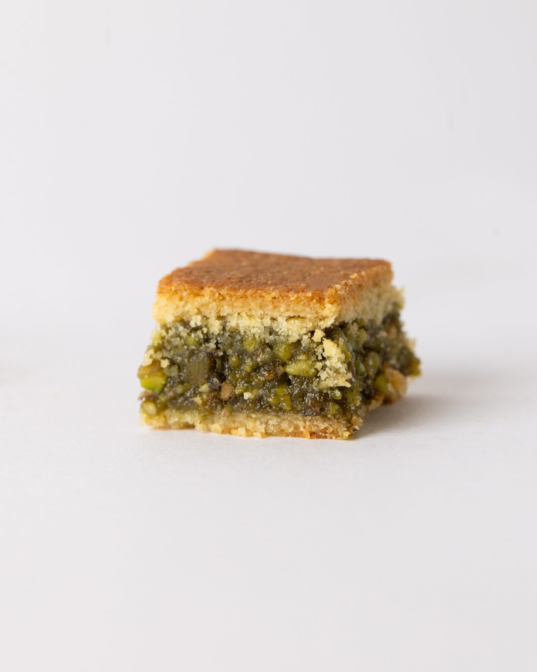 Close-up of a square piece of Maamoul mad pistachio with a golden semolina crust and ground pistachio filling.