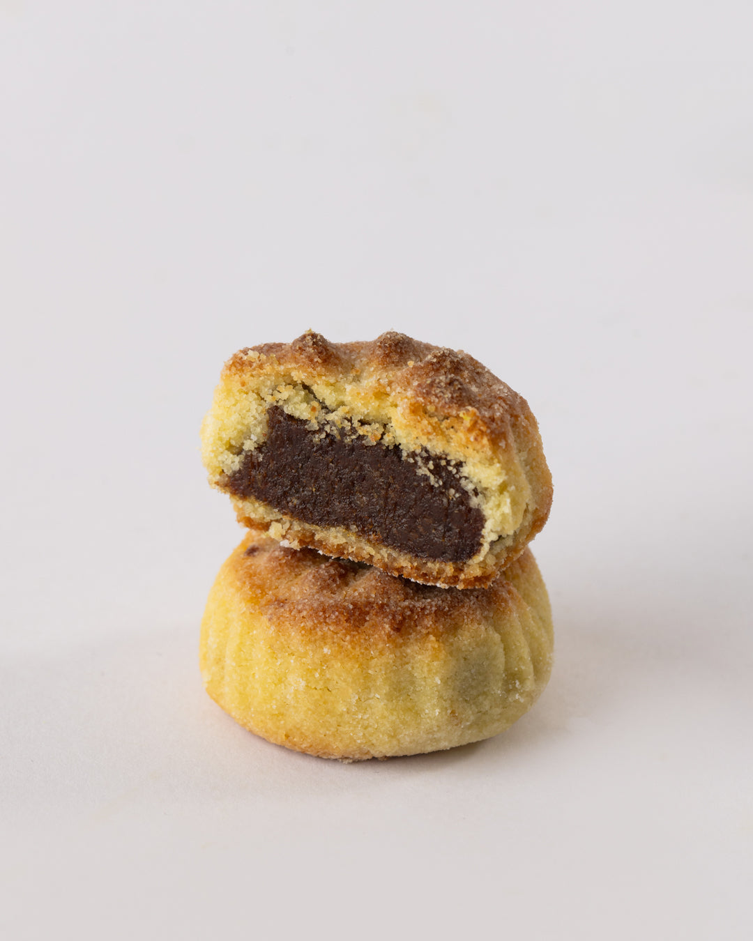Two Maamoul small tamer pastries, one whole and one cut open showing date filling inside on a white background.