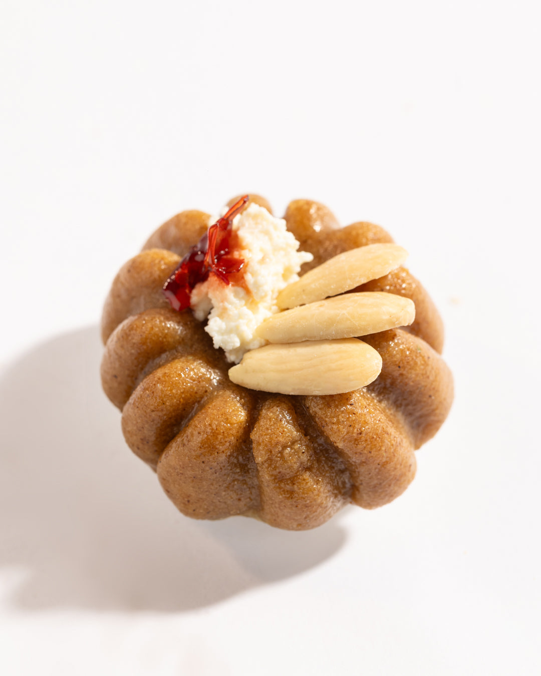 Close-up of a Mafrouke piece dessert topped with almonds, cream, and a touch of red jam on pistachio dough.