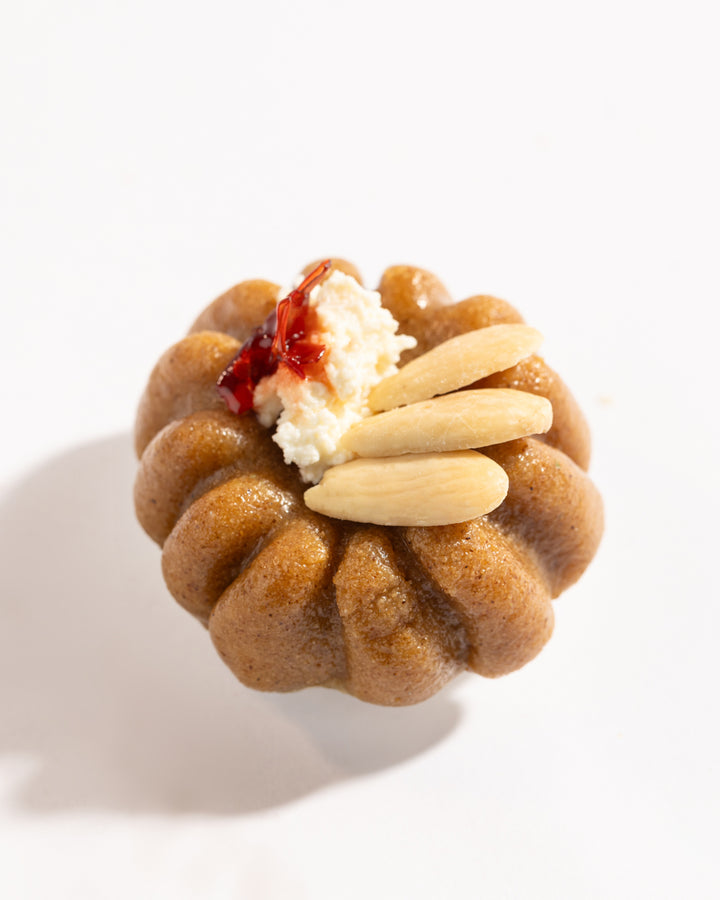 Close-up of a Mafrouke piece dessert topped with almonds, cream, and a touch of red jam on pistachio dough.