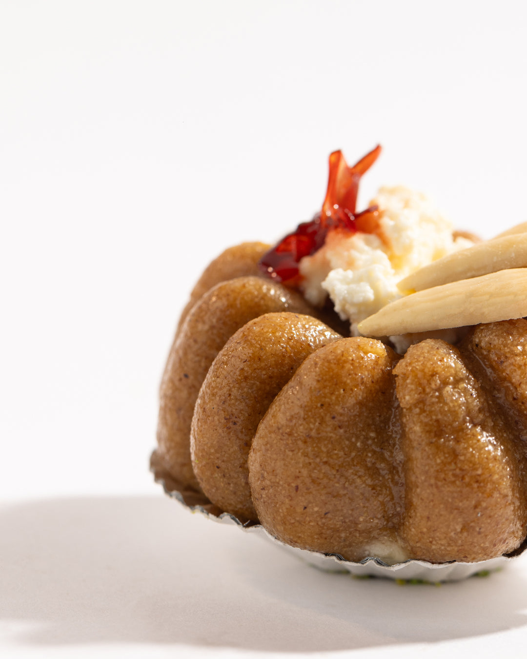 Close-up of a Mafrouke piece dessert with pistachio dough, creamy kashta filling, and pistachio topping on a white background.
