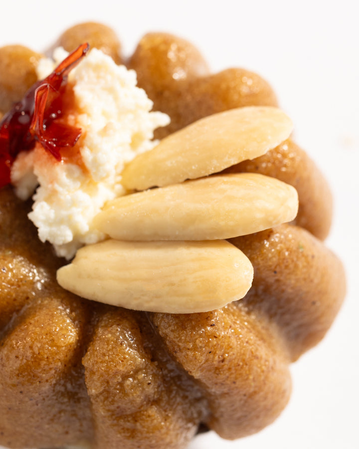 Close-up of a Mafrouke piece dessert topped with whole almonds, kashta cream, and a small dollop of red syrup.