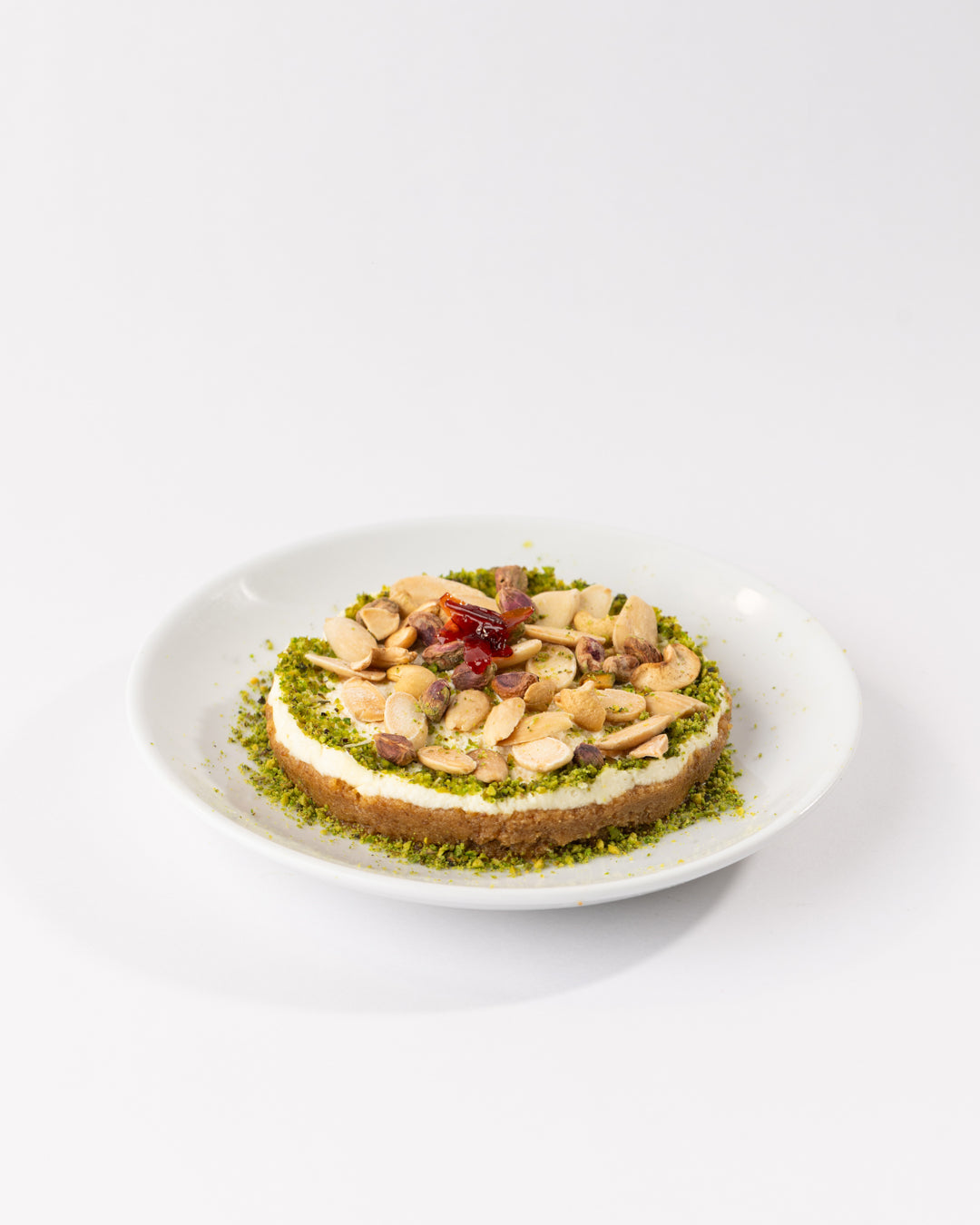 Mafrouke plate with roasted semolina base, creamy kashta, crunchy nuts, pistachio garnish, and floral jam drizzle on white plate.