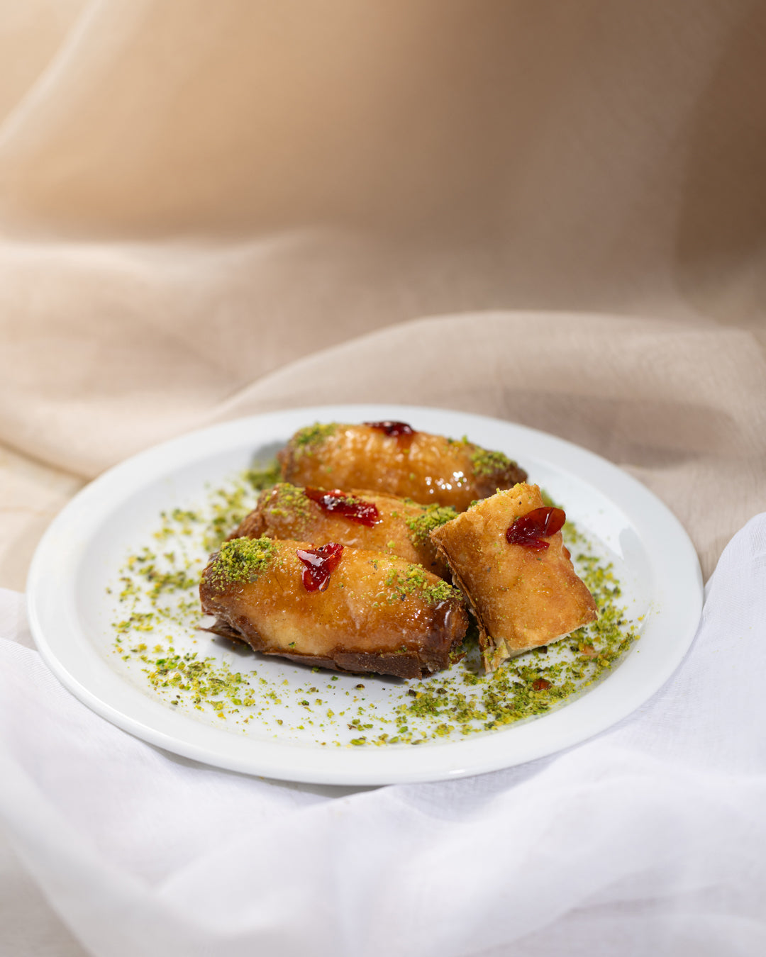 Golden-fried Znoud el set pastries with cream filling, drizzled syrup, garnished with crushed pistachios on a white plate