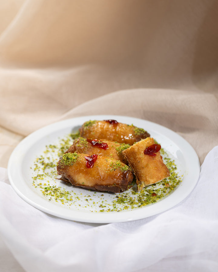 Golden-fried Znoud el set pastries with cream filling, drizzled syrup, garnished with crushed pistachios on a white plate