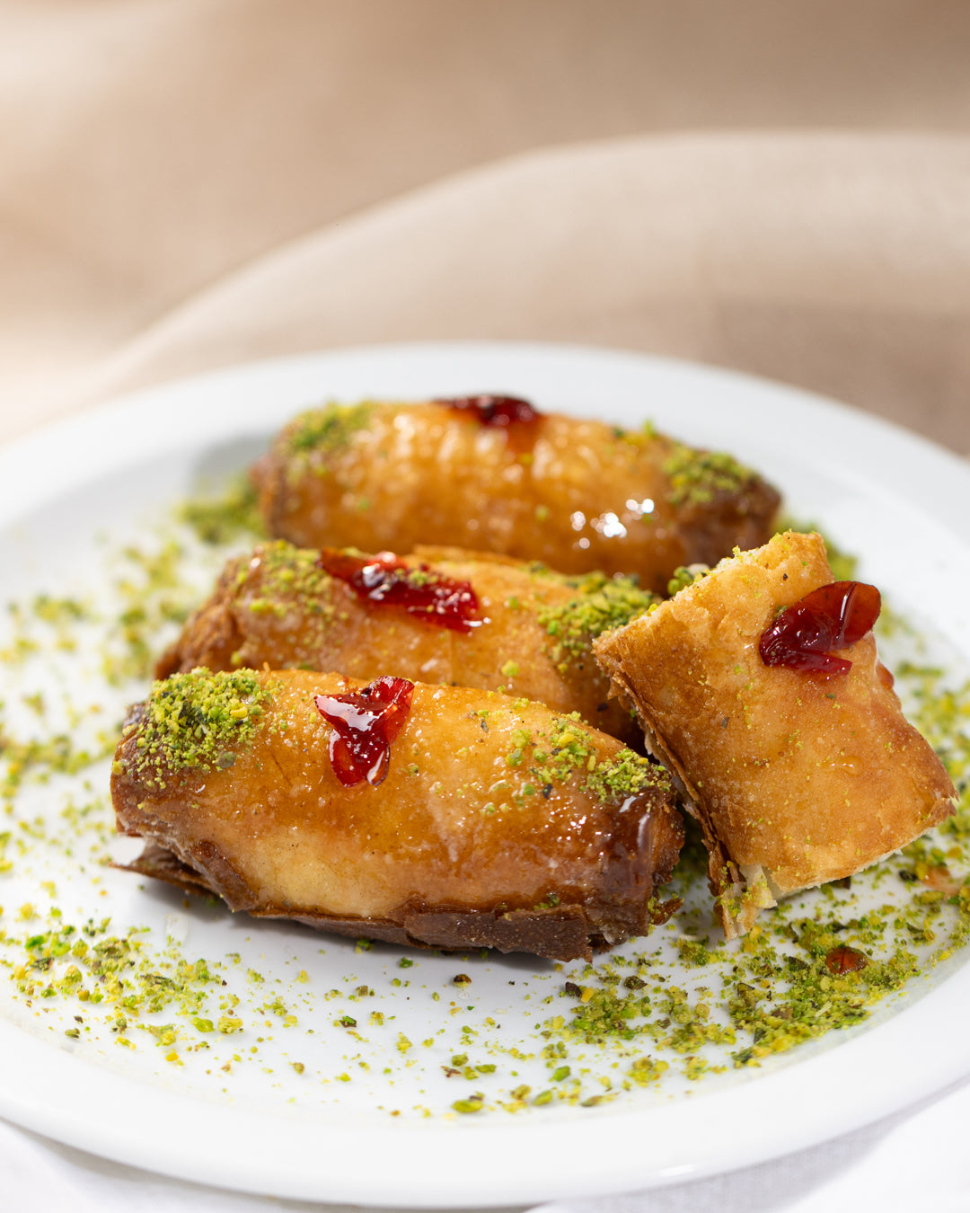 Golden fried Znoud el set pastries topped with pistachio crumbs and a dollop of red syrup on a white plate