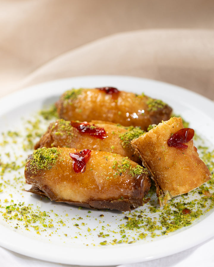 Golden fried Znoud el set pastries topped with pistachio crumbs and a dollop of red syrup on a white plate